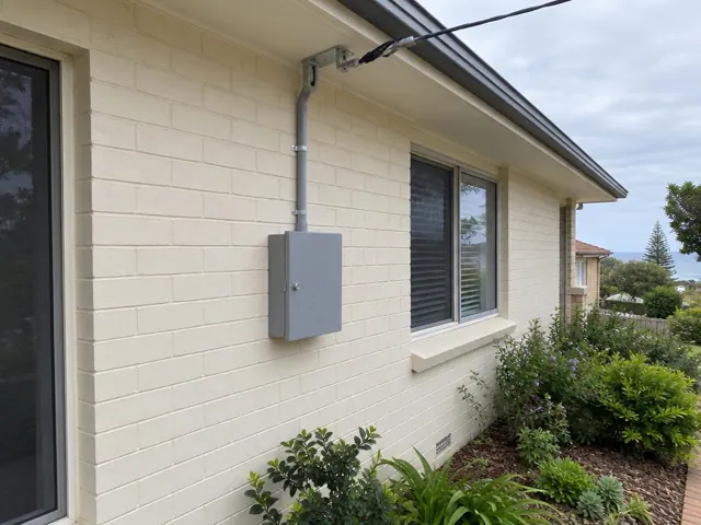 Cream brick house exterior with grey point-of-attachment bracket, overhead service cable and meter box in Pinny Beach